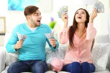 Happy couple sitting at home and counting money from the pig money box clipart