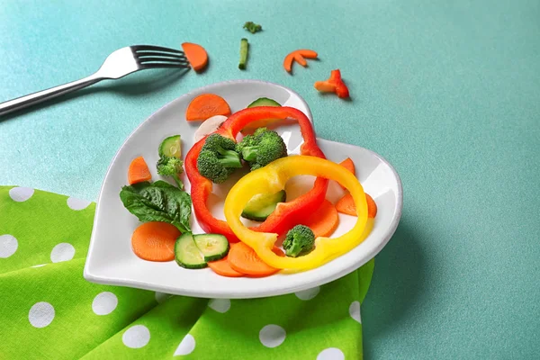 Useful cut vegetables on a plate in the form of heart on wooden table top view — Stock Photo, Image