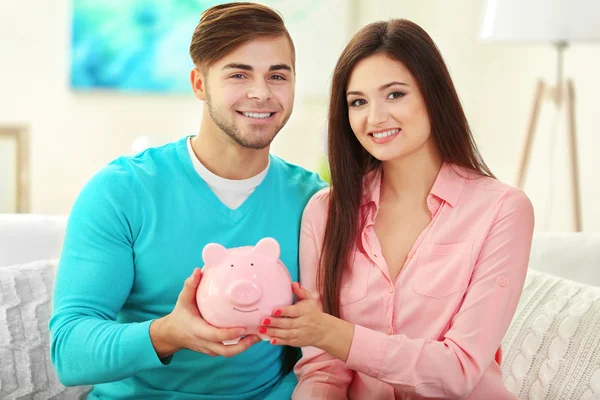 Pareja feliz sentada en casa y contando dinero de la caja de dinero de cerdo —  Fotos de Stock