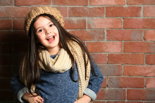 Porträt eines kleinen Mode-Mädchens mit Strickmütze und Schal auf Backstein-Hintergrund — Stockfoto