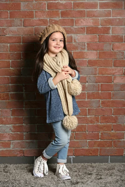 Portrait de petite fille de la mode enfant en bonnet tricoté et écharpe sur fond de mur de briques — Photo