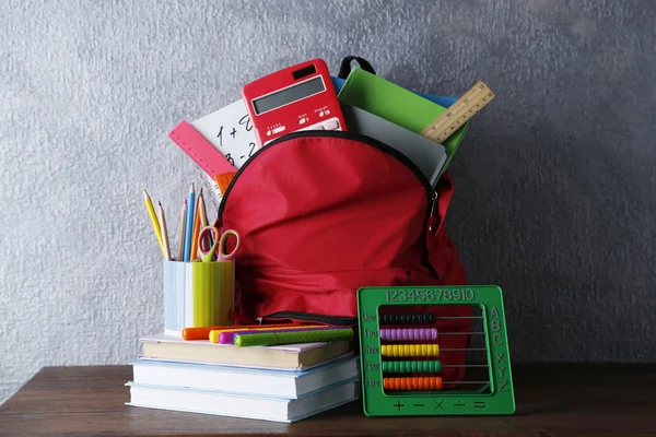 Mochila con útiles escolares en mesa de madera, sobre fondo de pared gris — Foto de Stock