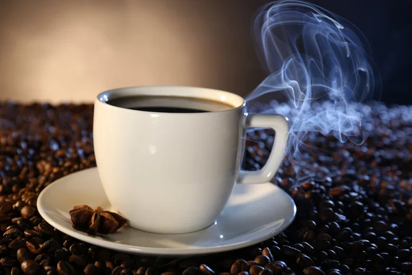 Kop warme koffie onder koffie bonen op donkere achtergrond — Stockfoto