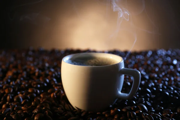 Xícara de café quente entre grãos de café no fundo escuro — Fotografia de Stock