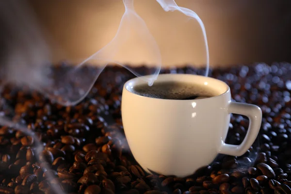 Kopp varm kaffe bland kaffebönor på mörk bakgrund — Stockfoto