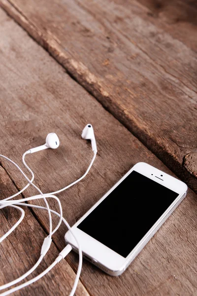 Celular branco com fones de ouvido em fundo de madeira — Fotografia de Stock