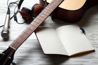 Akustik gitar, kulaklık, açılan not defteri ve ahşap arka plan üzerinde mikrofon yakın çekim