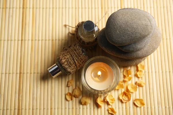 Belle composition avec bougie, huile d'arôme et cailloux sur tapis de bambou — Photo