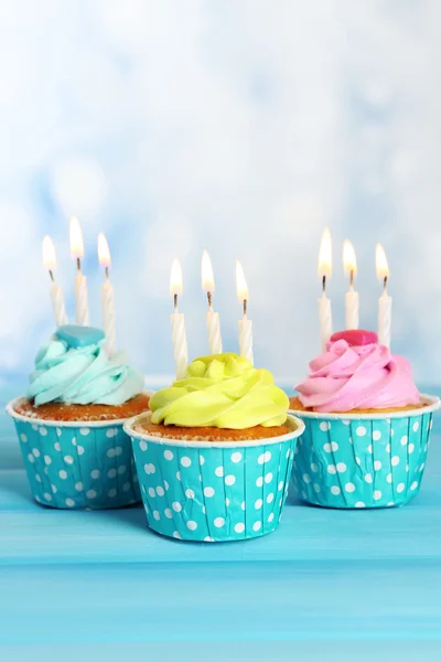 Leckere Cupcakes mit Kerzen auf blauem Holztisch vor verschwommenem Hintergrund — Stockfoto