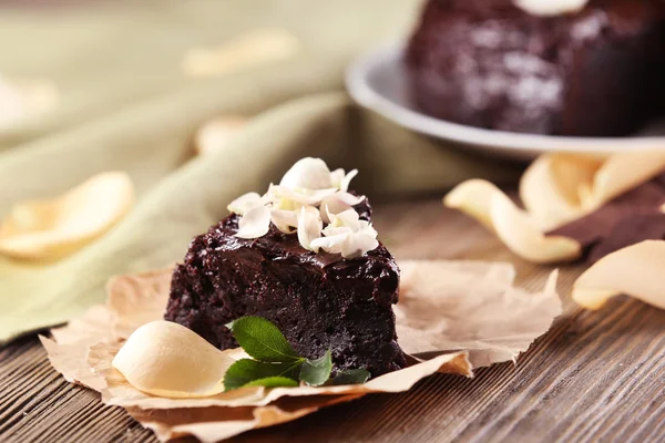 Kawałek ciasta czekoladowe, udekorowany kwiatami na brązowy drewniany stół — Zdjęcie stockowe