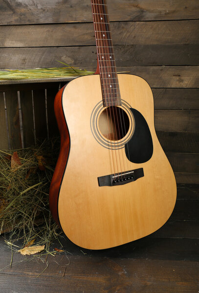 Acoustic guitar against box with hay on wooden background