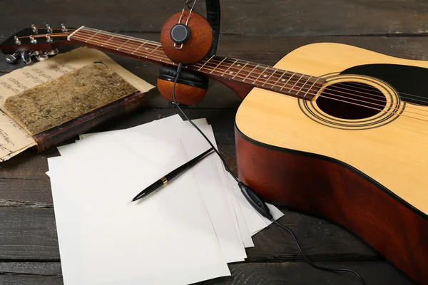 Chitarra acustica, cuffie, note musicali e white paper su fondo legno — Foto Stock