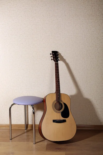 Guitarra acústica apoiada na parede com banquinho na sala — Fotografia de Stock