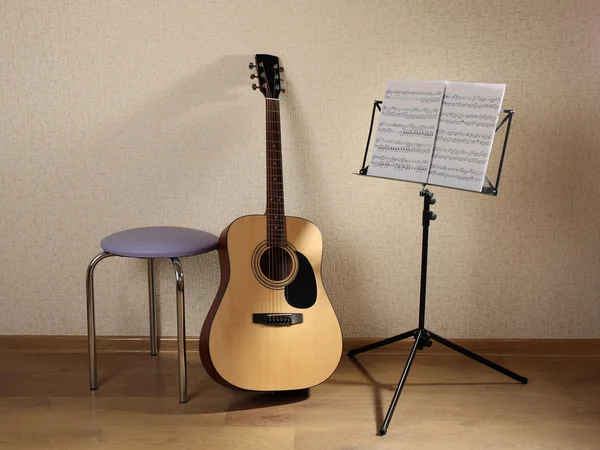 Acoustic guitar propped on wall with stool and musical notes holder in the room — Stock Photo, Image