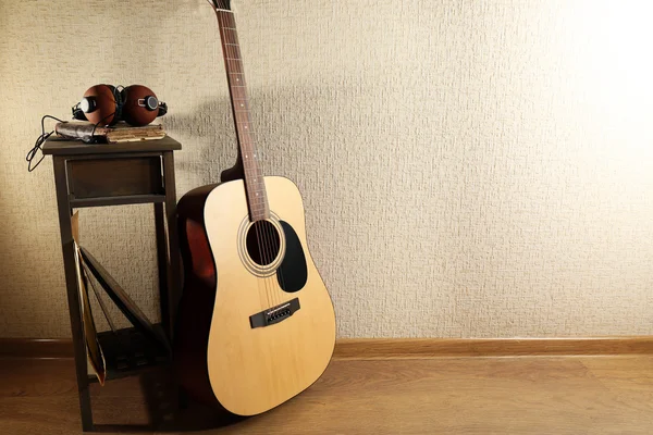Guitarra acústica apoyada en la pared con taburete y auriculares en la habitación, de cerca — Foto de Stock