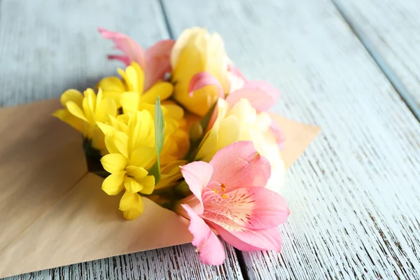 Fresh bouquet of flowers in envelope on wooden background — Stock Photo, Image