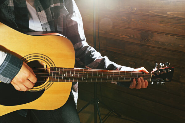 Guitarist plays guitar on wooden background, close up