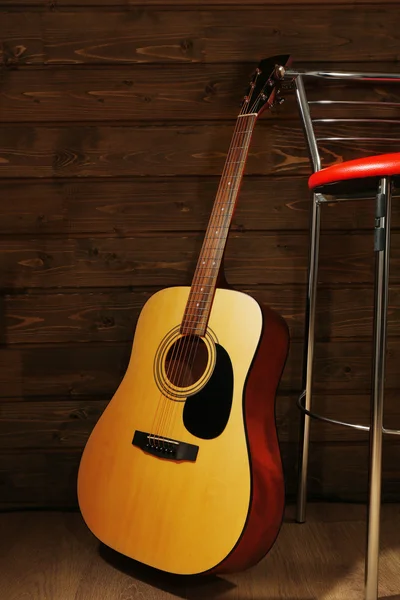Akustická kytara opřel o dřevěnou zeď s Barová židle v místnosti — Stock fotografie