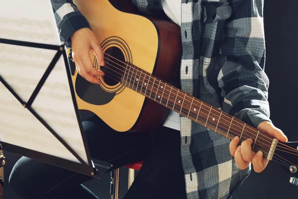 Músico toca la guitarra sobre fondo negro en estudio con soporte de notas musicales, de cerca — Foto de Stock