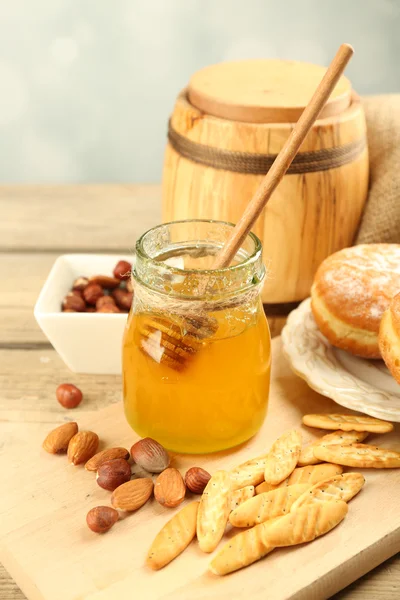 Botol kaca dengan madu, sarang madu dan kacang pada latar belakang kayu — Stok Foto