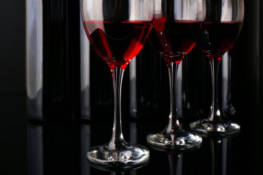 Şarap şişeleri üst üste siyah arka plan üzerine karşı gözlük, yakın çekim