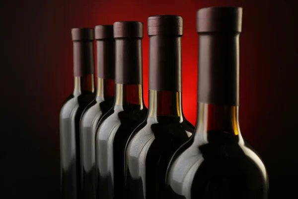 Weinflaschen in einer Reihe auf dunkelrotem Hintergrund, Nahaufnahme — Stockfoto