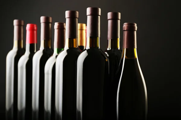 Wino butelki z rzędu na ciemnym tle, z bliska — Zdjęcie stockowe