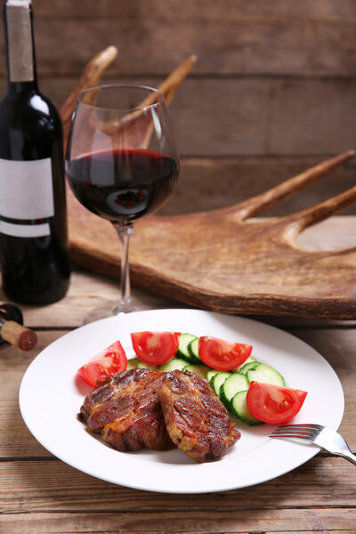 Roasted venison fillet and fresh vegetables on plate, on wooden background