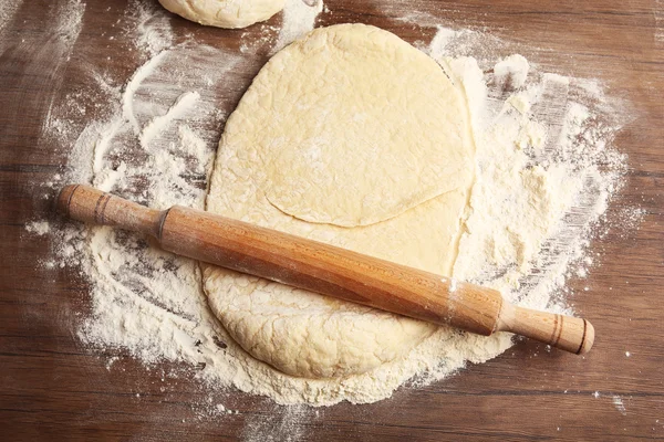 Dough for pizza and rolling-pin on wooden table — Stock Photo, Image