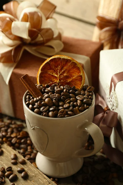 Beautiful gift with bow and coffee grains in mug, on wooden background — Stock Photo, Image