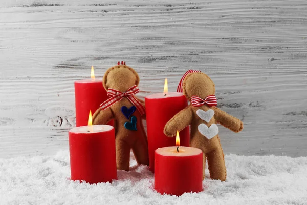 Filzpuppen und rote Kerzen im Schnee vor hölzernem Hintergrund, Stillleben — Stockfoto
