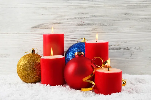 Red candles with colorful baubles in a snow over wooden background, still life — Stock Photo, Image