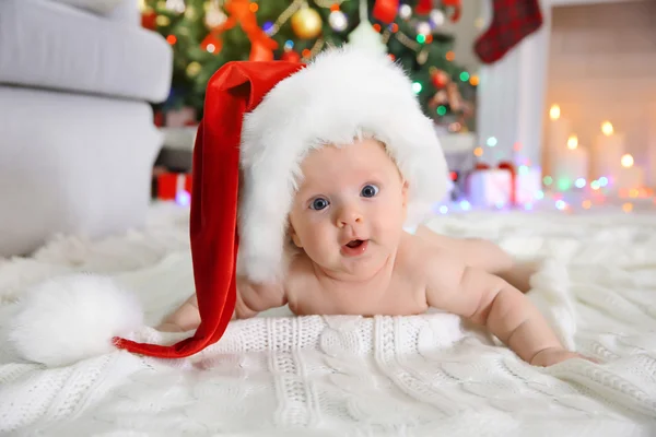 Nacktes Baby mit rotem Hut auf dem Boden im geschmückten Weihnachtszimmer — Stockfoto