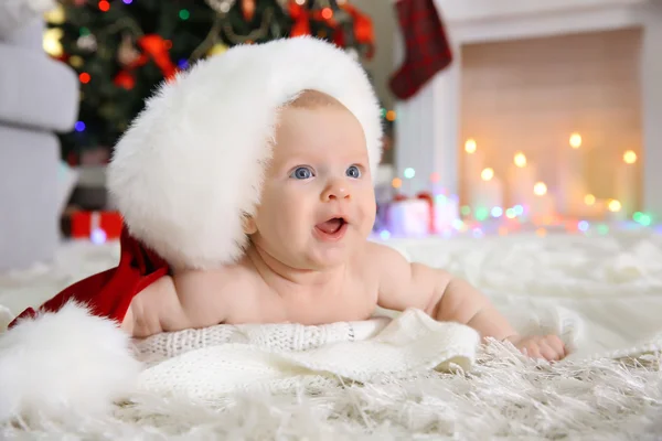 Nacktes Baby mit rotem Hut auf dem Boden im geschmückten Weihnachtszimmer — Stockfoto