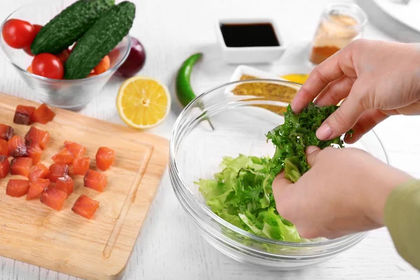 Mani femminili che aggiungono foglie di lattuga in ciotola con insalata, primo piano — Foto Stock