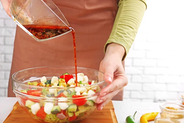 Proces van de voorbereiding van de saus voor salade, op keuken. Vrouw gieten saus in glazen kom met salade ingrediënten — Stockfoto