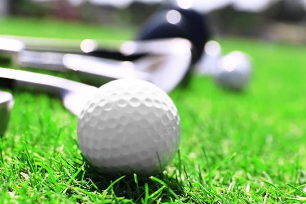 Clubes de golfe diferentes em uma fileira e bolas em uma grama verde, close-up — Fotografia de Stock