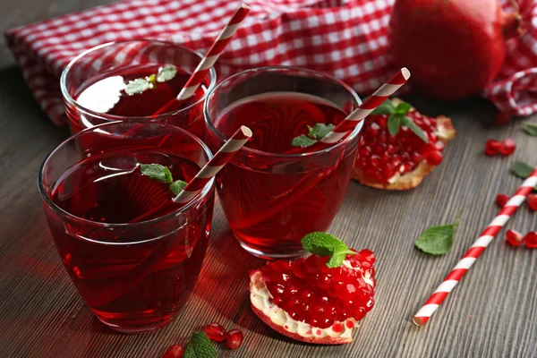 Three glasses of tasty juice and garnet fruit, on wooden background — Stock Photo, Image