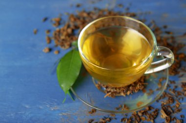 Cam bardak çay yeşil yaprakları ile ve mavi ahşap arka plan etrafında dağınık çay
