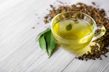 Cam bardak çay yeşil yaprakları ile ve gri ahşap arka plan üzerinde etrafında dağınık çay yakın çekim