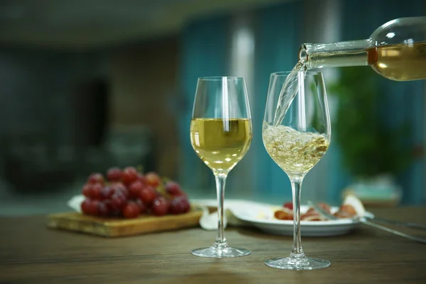 Gießen von Weißwein aus der Flasche in das Weinglas auf dem Tisch vor verschwommenem Hintergrund — Stockfoto