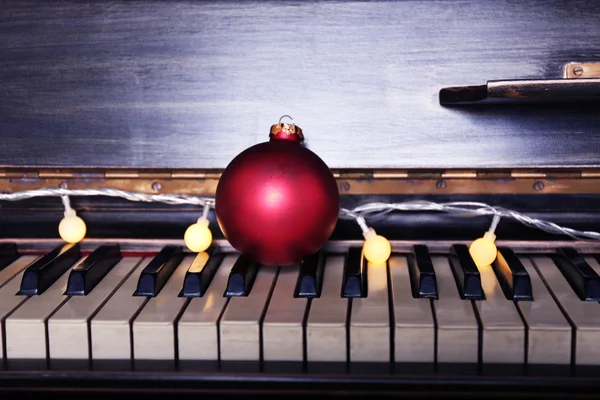 Teclas de piano decoradas com luzes de decoração e bola vermelha, close-up — Fotografia de Stock