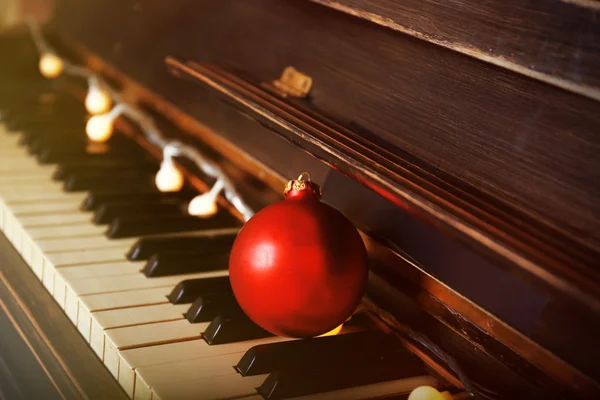 Teclas de piano decoradas com luzes de decoração e bola vermelha, close-up — Fotografia de Stock