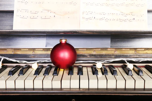 Tasti di pianoforte decorati con luci di decorazione e palla rossa, primo piano — Foto Stock