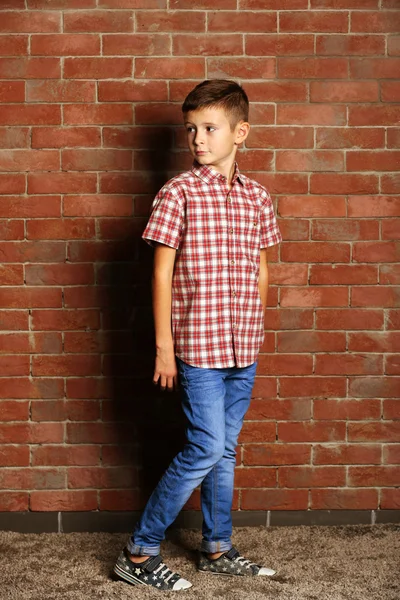 Schattige kleine jongen op bakstenen muur achtergrond. Kinderen mode concept — Stockfoto