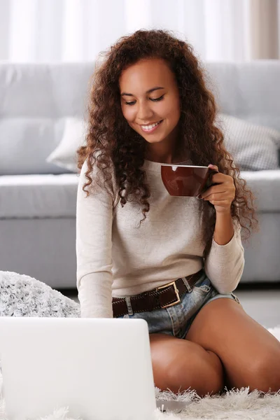 年轻漂亮的女人，地上使用笔记本电脑，在白色背景上喝咖啡 — 图库照片