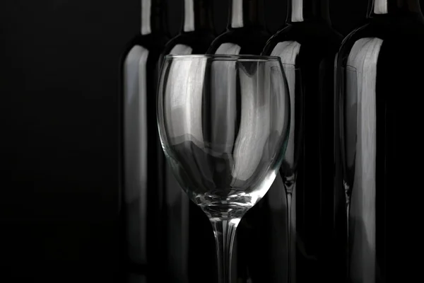 Bouteilles de verre et de vin en rangée sur fond noir, gros plan — Photo