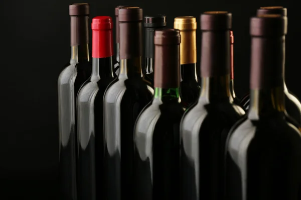 Botellas de vino en fila sobre fondo negro, de cerca — Foto de Stock