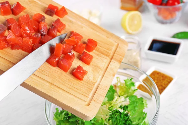 Mãos femininas adicionando pedaços de salmão em tigela com salada, close-up — Fotografia de Stock
