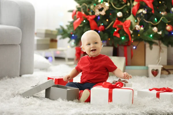 Смешной ребенок с подарочными коробками и елкой на заднем плане — стоковое фото